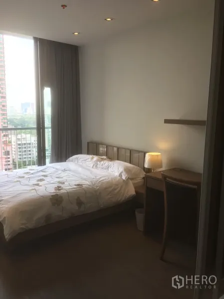 Condominium for rent or sale in Khlong Toei, Bangkok - Bright bedroom with queen bed, desk and a balcony overlooking the city skyline.
