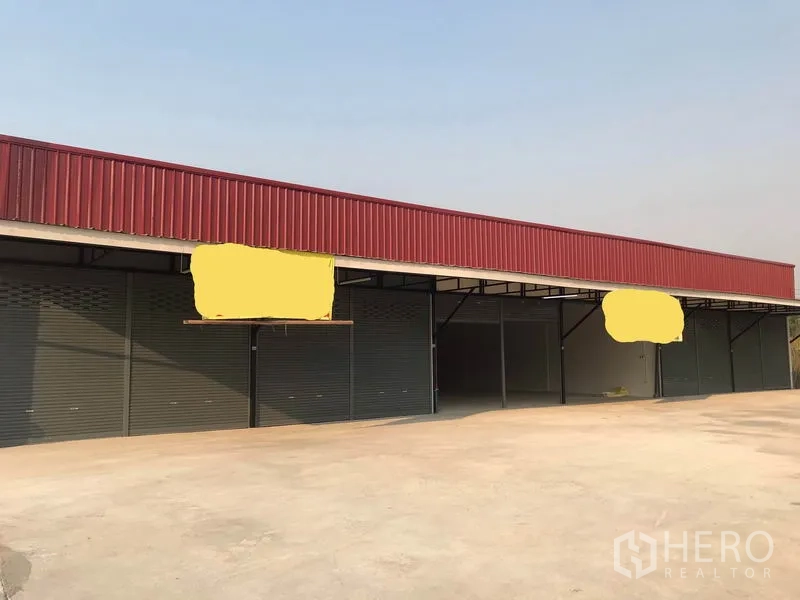 Warehouse for rent in Lam Luk Ka, Pathum Thani - Front elevation of low-rise warehouse row with red fascia and several roller shutters.