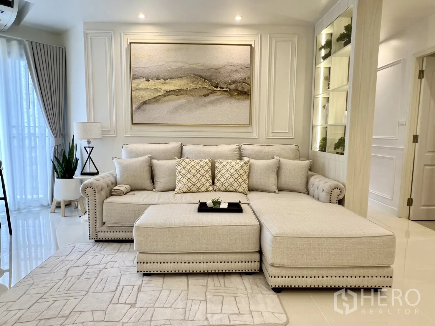 Condominium for rent in Yan Nawa, Bangkok - Front view of plush sectional sofa with wall art and illuminated display shelves.