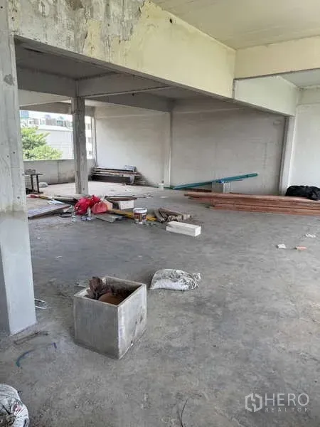 Shophouse for rent in Watthana, Bangkok - Spacious unfinished floor plate with columns and building supplies ready for refurbishment.