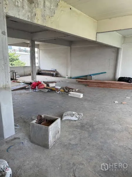 Shophouse for rent in Watthana, Bangkok - Spacious unfinished floor plate with columns and building supplies ready for refurbishment.