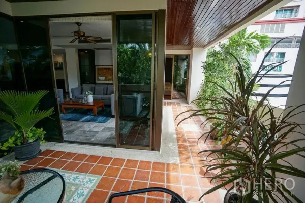 Apartment for rent in Watthana, Bangkok - Wraparound terrace with terracotta tiles and greenery outside the living room’s glass doors.