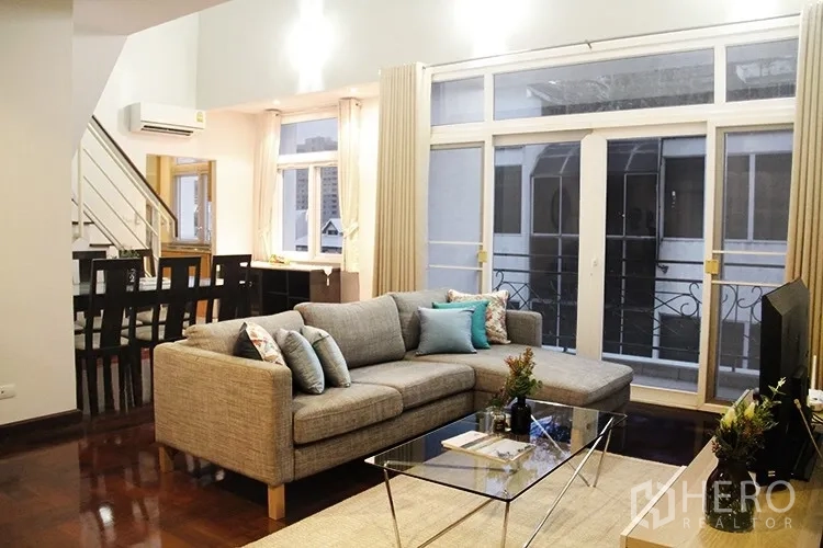 Apartment for rent in Khlong Toei, Bangkok - Open-plan lounge with L-shaped sofa, glass coffee table and balcony doors