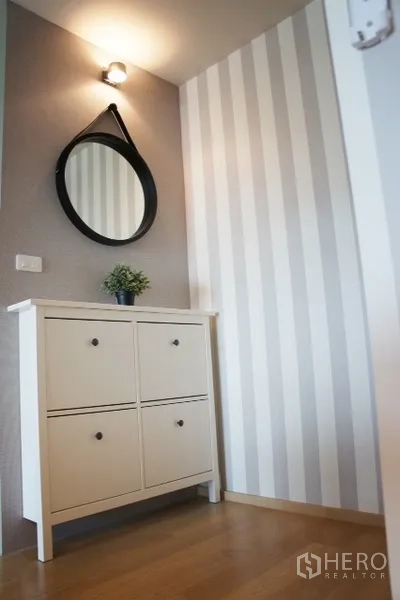 Condominium for rent in Phaya Thai, Bangkok - Entry nook with white shoe cabinet, round mirror, striped feature wall and warm wood flooring.