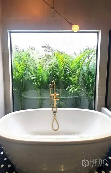 带办公室的家 出租或出售在Khlong Toei, Bangkok - 浴室设独立浴缸与黄铜龙头，大窗外即葱郁绿植。