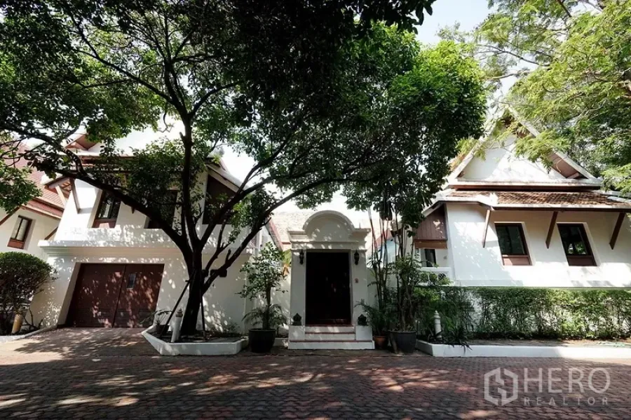 独立式住宅 出租在Watthana, Bangkok - 泰式风格独栋别墅正门，带车库与成树庭院，砖石铺装车道。
