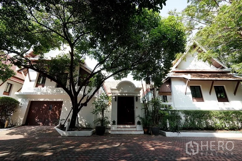 独立式住宅 出租在Watthana, Bangkok - 泰式风格独栋别墅正门，带车库与成树庭院，砖石铺装车道。