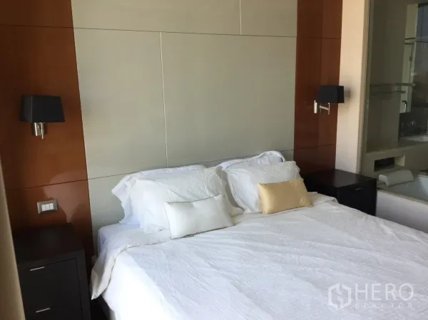 Condominium for rent in Khlong Toei, Bangkok - Bedroom with white bedding, wood panel headboard, wall sconces and twin nightstands.