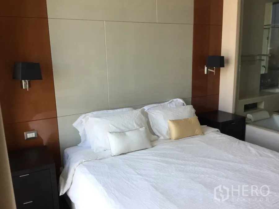 Condominium for rent in Khlong Toei, Bangkok - Bedroom with white bedding, wood panel headboard, wall sconces and twin nightstands.