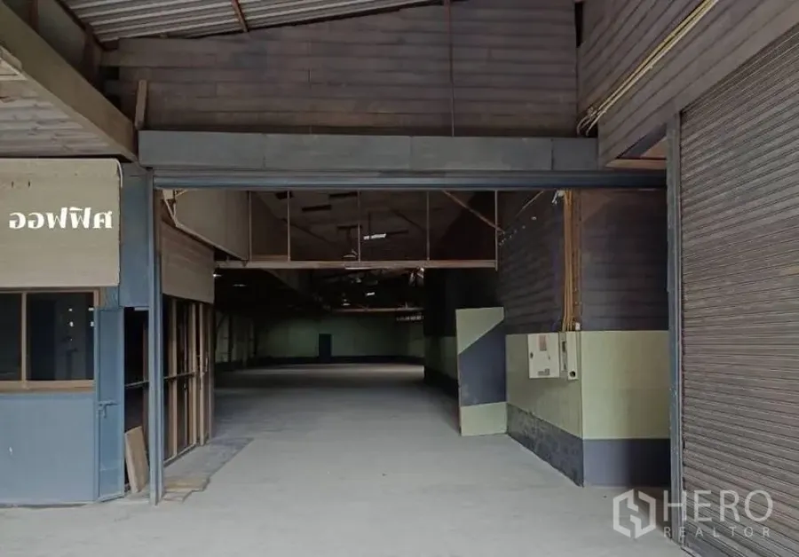 货栈 出租在Bang Khen, Bangkok - 曼谷邦肯仓库入口，卷帘门、办公室小隔间与宽阔混凝土地面。