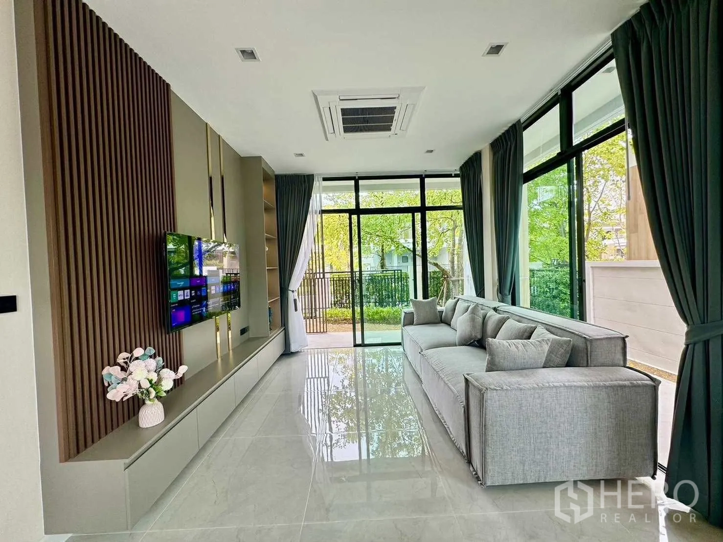 独栋房屋 for rent in Bang Phli, Samut Prakan - 采光充足的客厅，长形沙发、电视墙与大面积窗户望向绿景。