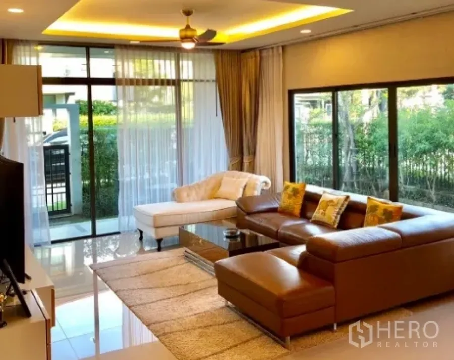 Detached House for rent in Bang Kapi, Bangkok - Bright living room with floor-to-ceiling windows, L-shaped leather sofa, chaise lounge and garden views.
