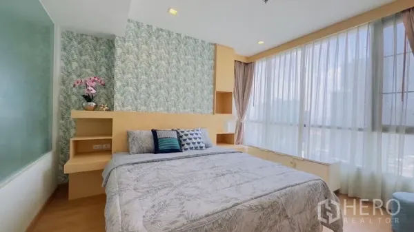 Condominium for rent in Watthana, Bangkok - Master bedroom with corner windows, sheer curtains and built-in headboard shelving.