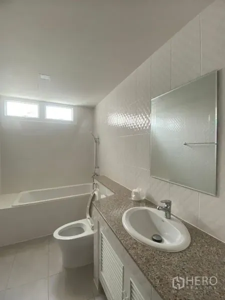 Condominium for rent in Sathon, Bangkok - Clean bathroom with bathtub, granite countertop vanity, sink, mirror, and high windows for natural light.