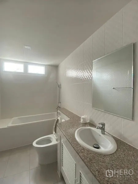 Condominium for rent in Sathon, Bangkok - Clean bathroom with bathtub, granite countertop vanity, sink, mirror, and high windows for natural light.