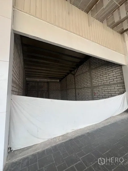 Retail Space for rent in Khlong Toei, Bangkok - Wide shopfront under canopy with partial tarp, concrete forecourt, and raw interior beyond.