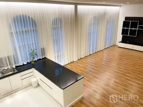 Townhouse for rent in Yan Nawa, Bangkok - Open-plan living area with wood floors and a wall of arched windows, adjoining kitchen with stone counter.