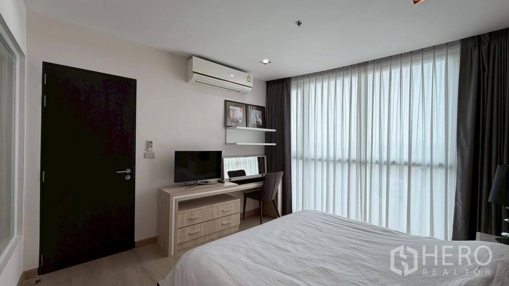 คอนโด for rent or sale in Watthana, Bangkok - มุมห้องนอนพร้อมทีวีบนโต๊ะทำงาน ชั้นลอย แอร์ และม่านโปร่งบนหน้าต่างสูง