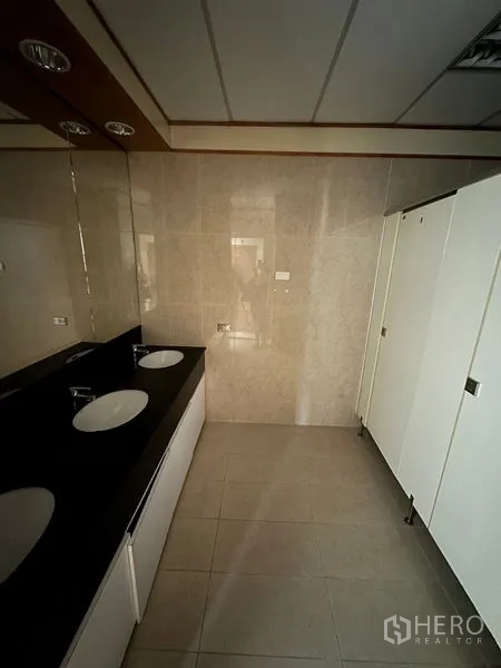 Office Space for rent in Pathum Wan, Bangkok - Modern restroom with black countertop, double sinks, large mirror, tiled walls, and white partitioned stalls.
