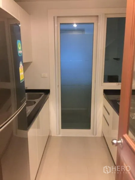 公寓 出租或出售在Khlong Toei, Bangkok - 封闭式现代厨房，黑色台面、水槽、冰箱与推拉玻璃门。