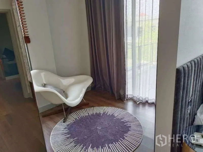 Detached House for rent in Bang Phli, Samut Prakan - Cozy reading nook with sculptural white lounge chair, purple round rug and sheer drapes by a window.