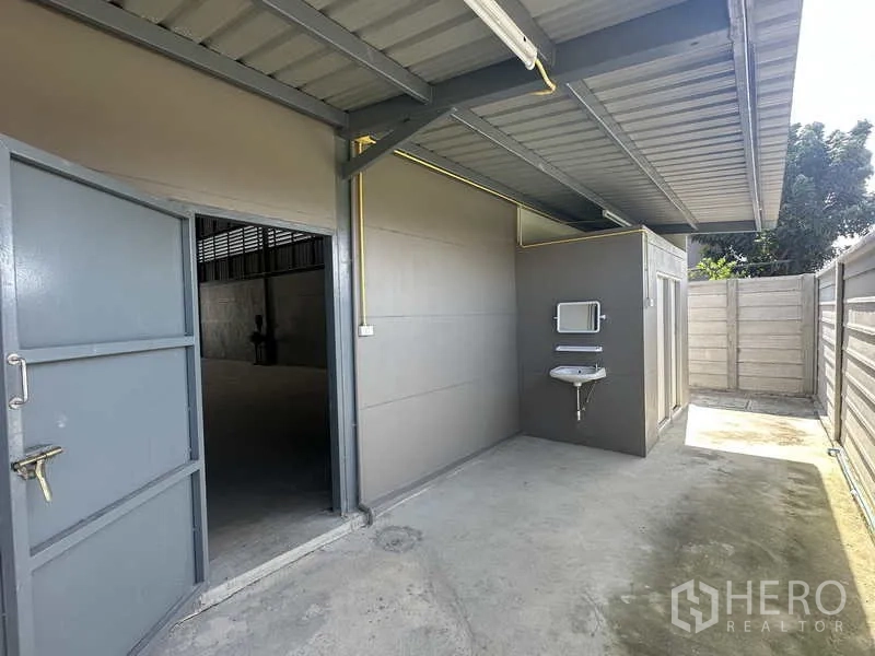 Warehouse for rent in Bang Bua Thong, Nonthaburi - Side service zone with entrance door, sink and a covered utility area beside the warehouse.