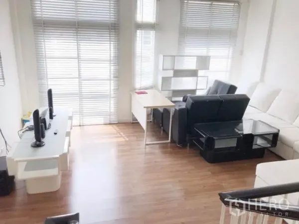 Townhouse for rent in Prawet, Bangkok - Bright living area with large windows, blinds, wood flooring, black and white sofas, and a work desk.