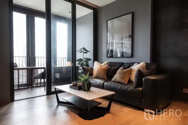 Condominium for rent in Khlong Toei, Bangkok - Contemporary lounge with black leather sofa, coffee table and sliding glass partition leading to a study area.