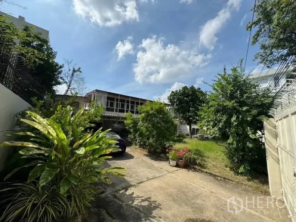 独立式住宅 出租在Watthana, Bangkok - 宽敞前院与车道，绿树成荫，通往一栋独立屋，蓝天晴朗。