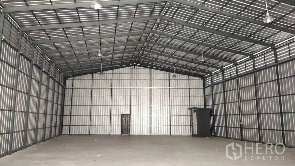 Warehouse for rent in Bang Lamung, Chon Buri - Empty warehouse showing insulated metal walls, side ventilation panels, hanging lights and tall ceiling.