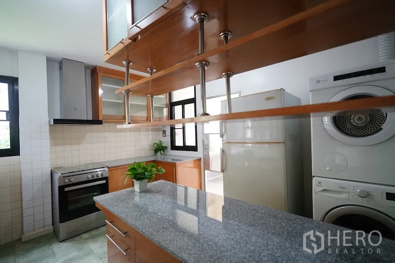 Detached House for rent in Chatuchak, Bangkok - Kitchen view with stone island, open shelving, range, refrigerator, and stacked washer dryer.