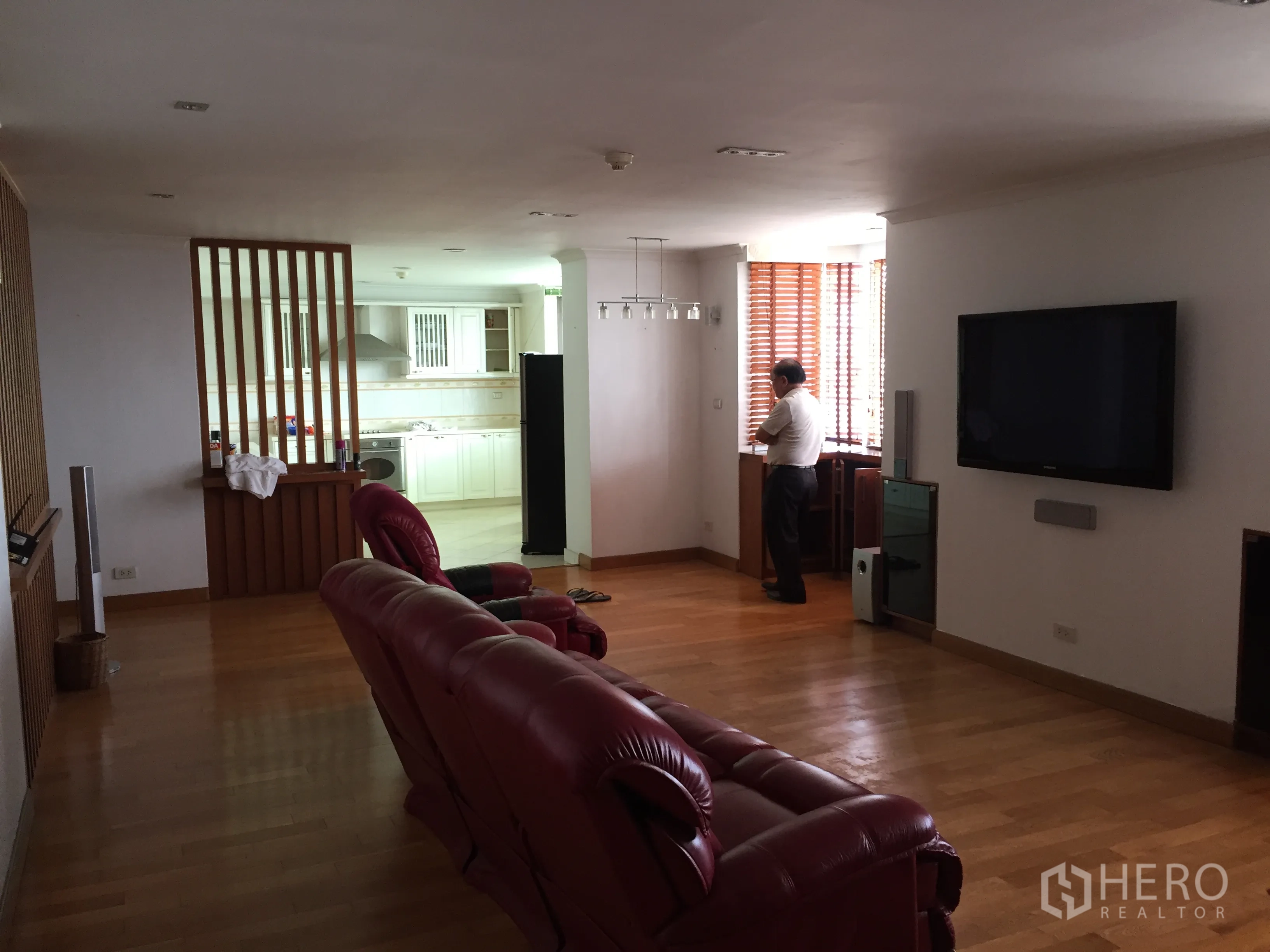 Condominium for rent in Khlong Toei, Bangkok - Open-plan living area with TV wall, wood flooring and sightline into the white kitchen.