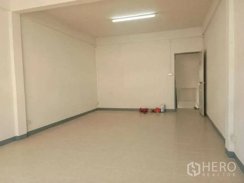 Shophouse for rent in Bang Na, Bangkok - Open-plan ground floor with tiled flooring, white walls and fluorescent lighting.