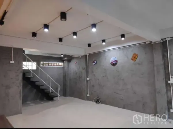 Home Office for rent in Khlong Toei, Bangkok - Open-plan ground floor with polished concrete walls, ceiling spotlights, and a metal staircase.