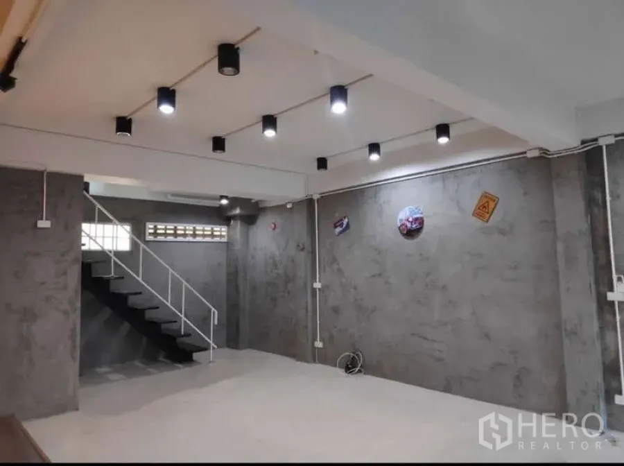 Home Office for rent in Khlong Toei, Bangkok - Open-plan ground floor with polished concrete walls, ceiling spotlights, and a metal staircase.