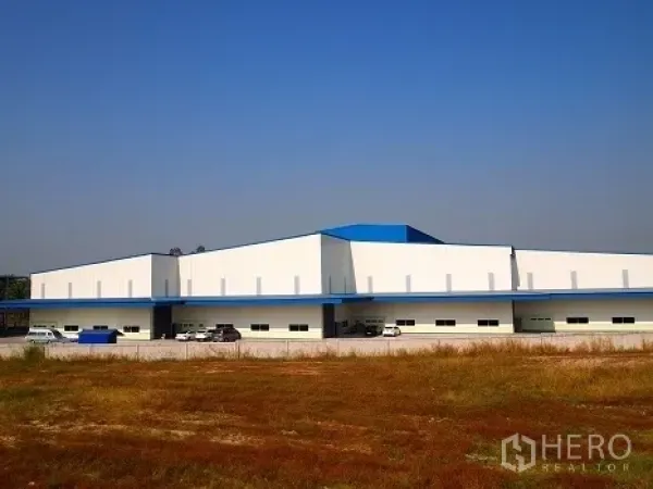 โรงงาน ให้เช่าในSi Racha, Chon Buri - ภาพมุมกว้างตัวอาคารโรงงานชั้นเดียวสีขาวหลังคาสีน้ำเงิน มีที่จอดรถ มองจากพื้นที่โล่ง