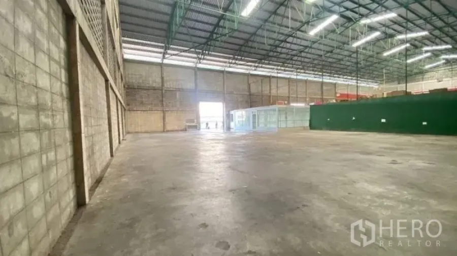 Warehouse for rent in Prawet, Bangkok - Spacious warehouse interior with high steel truss roof, concrete floor, wide shutter entry and a glass-front office room.