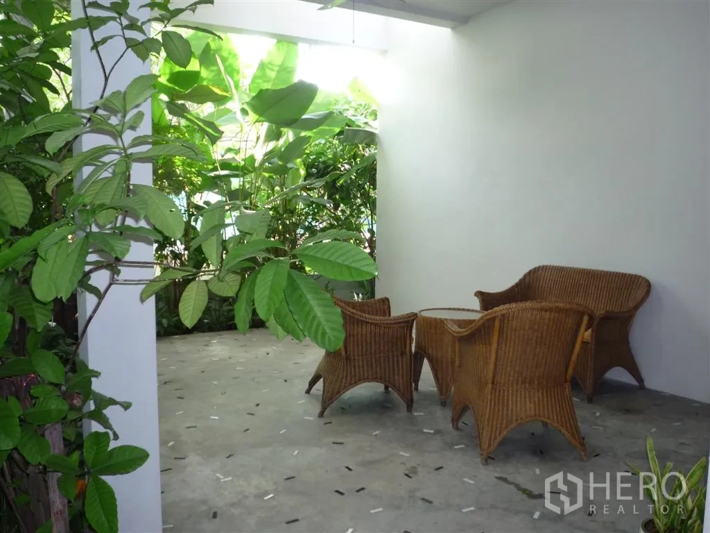 Detached House for rent in Khan Na Yao, Bangkok - Shaded outdoor terrace with rattan chairs and table facing greenery.