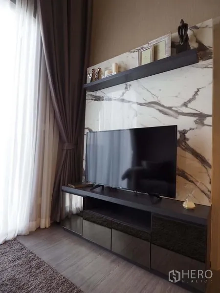 Condominium for rent in Khlong San, Bangkok - TV console against a marble feature wall with floating shelf and tall curtains.