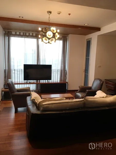 Condominium for rent or sale in Khlong Toei, Bangkok - Bright living area with floor-to-ceiling windows, TV stand and chandelier in a Bangkok condo.