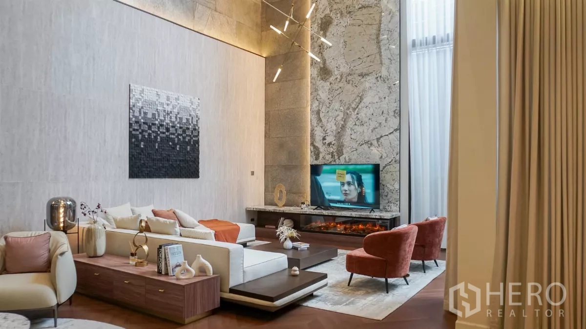 Detached House for rent or sale in Bang Kapi, Bangkok - Living area with sectional sofa, marble TV wall, fireplace shelf and accent armchairs.