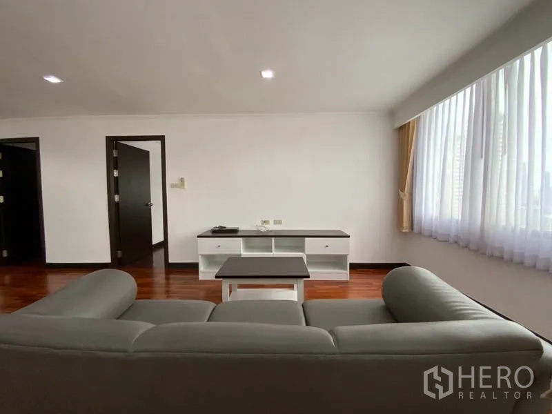 公寓 出租在Watthana, Bangkok - 极简客厅，灰色沙发、电视柜，宽窗带来充足采光，木地板光洁。