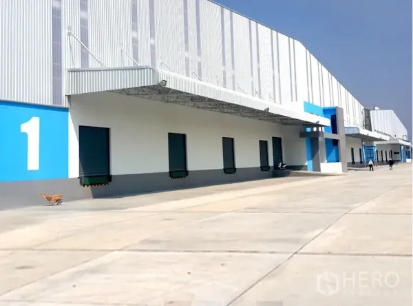 货栈 出租在Chachoengsao - 一排带雨棚的装卸月台，卷帘门通向仓库。