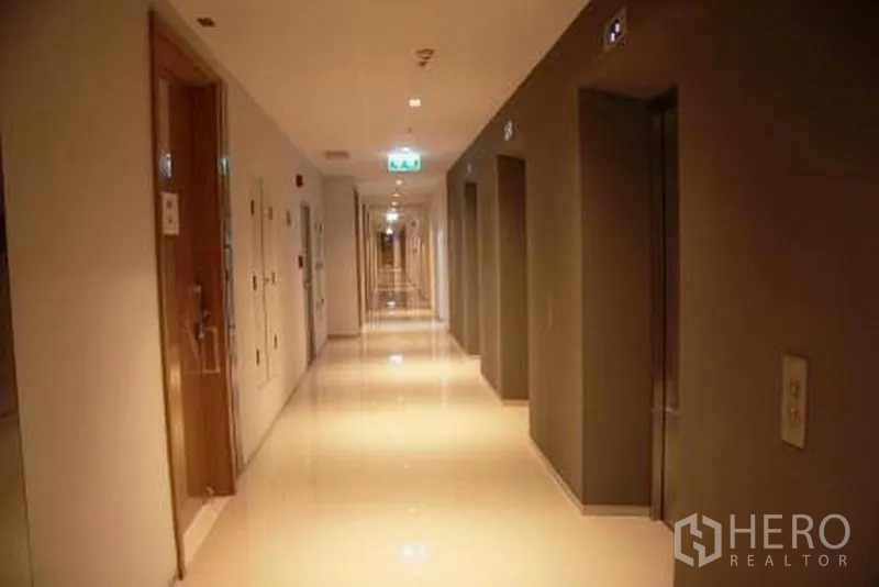 Condominium for rent or sale in Watthana, Bangkok - Well-lit condominium corridor with glossy tile flooring, unit doors and elevator bays.