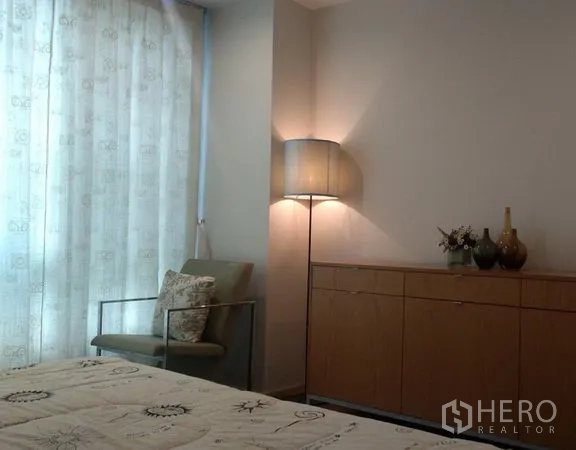 公寓 出租在Khlong Toei, Bangkok - 卧室一角有扶手椅、边柜与柔和落地灯，旁为带帘窗户。