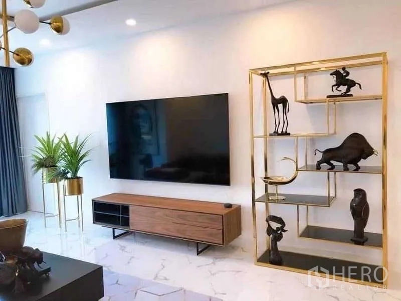 公寓 出租或出售在Watthana, Bangkok - 电视背景墙，大屏电视、金色展示架与室内绿植。
