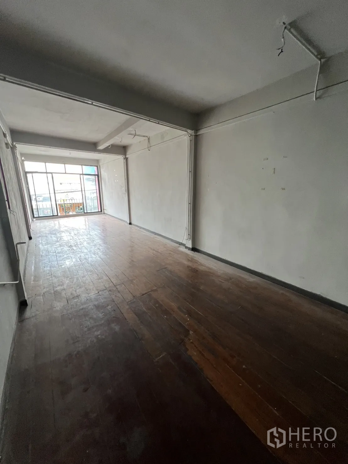 Shophouse for rent in Watthana, Bangkok - Open-plan upper floor with worn wood floors and sliding doors to balcony.