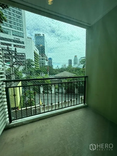 Condominium for rent in Khlong Toei, Bangkok - Covered balcony with safety net overlooking city buildings and treetops.