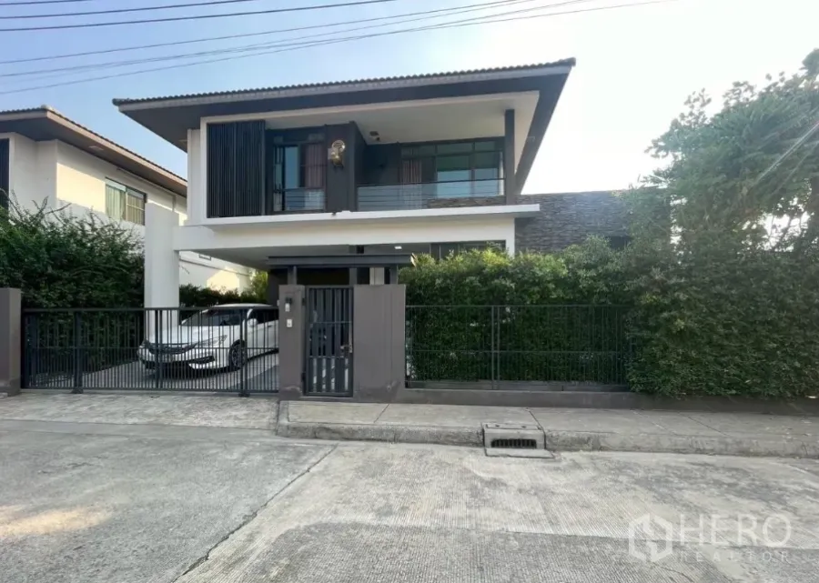บ้าน ขายในBang Phli, Samut Prakan - บ้านเดี่ยวสองชั้นสไตล์โมเดิร์น รั้วเหล็กและที่จอดรถหน้าบ้าน พร้อมแนวไม้พุ่มบนแปลงมุม