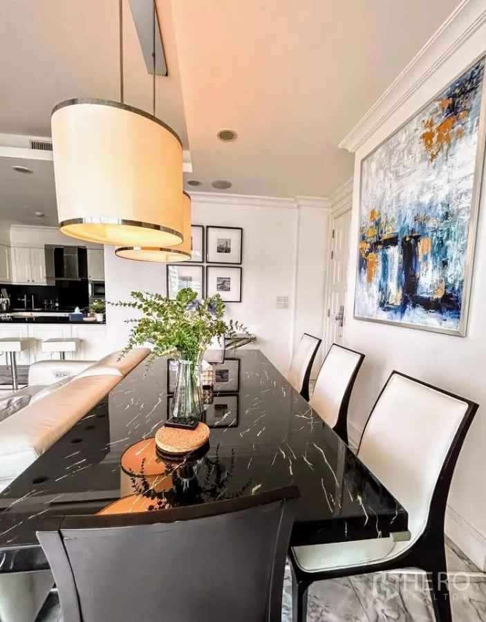 Condominium for sale in Watthana, Bangkok - Elegant dining space with black marble table, modern pendant lights and artwork, beside a bright kitchen.